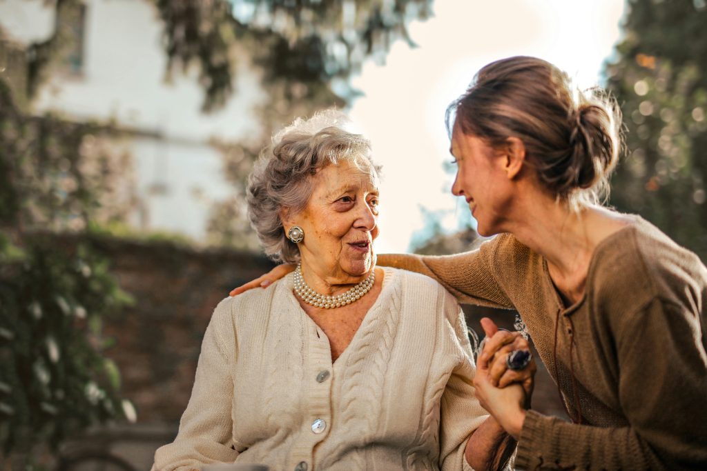 Omsorgsfuld kvinde smiler, mens hun hjælper en ældre kvinde i kørestol